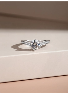 Close-up of six-prong moissanite ring on beige stone stand showing side diamond details
