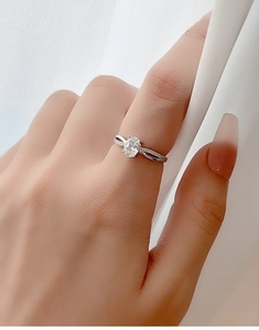 Makroaufnahme eines ovalen Zirkonia-Rings am Finger mit überkreuztem Diamantband