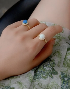 Detailed shot of gold Cuban link rings with blue and white opal stones on patterned fabric