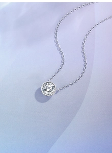 Macro shot of 1ct round moissanite pendant on silver chain against purple satin