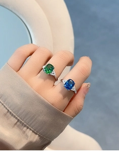 Close-up of S925 silver rings with cushion-cut blue sapphire and emerald gemstones