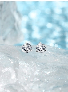 Macro shot of sparkling three-prong moissanite stud earrings resting on crystal clear ice