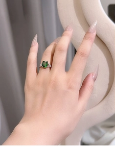 Close-up of radiant cut green gemstone ring with side diamond accents on finger