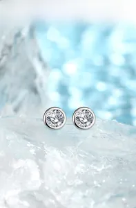 Detailed close-up of Moissanite stud earrings in silver bezel setting on ice background