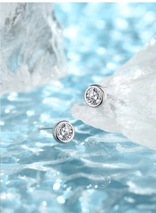Macro shot of silver bezel-set moissanite stud earrings on sparkling ice background