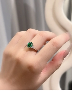 Detailed view of an oval green sapphire ring on hand with elegant side diamonds