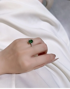 Close-up of an oval green gemstone ring in silver set on a model's hand with white fabric
