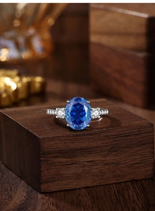Macro shot of Radiant-cut royal blue sapphire ring on a wooden stand with bokeh lights