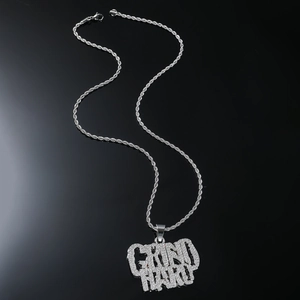 Macro view of iced out silver GRIND HARD letter pendant with sparkling crystal details