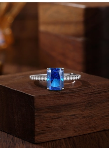 Macro shot of Radiant-cut Royal Blue sapphire ring on wooden stand showing silver band detail