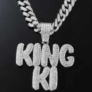 Macro detail of iced-out KING KI hip hop pendant with sparkling white zircons on silver chain