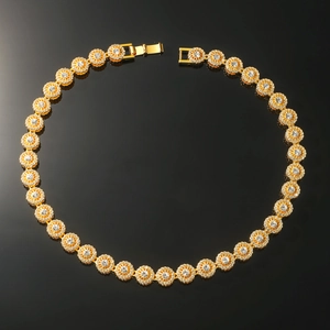 Macro detail of gold flower link necklace with pave set crystals on dark background