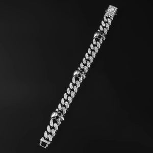 Detailed view of silver Cuban link chain with crystal skull charms on black surface