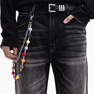 Détail d'une chaîne de pantalon en perles colorées accrochée à un jean en denim délavé