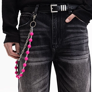 Détail d'une chaîne de pantalon à perles roses et maillons argentés sur un jean
