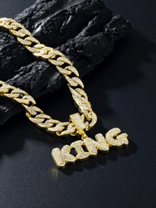 Macro detail of gold Cuban link chain with iced-out KING pendant on dark stone base