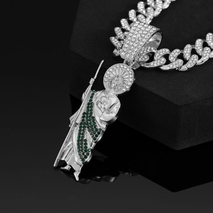 Macro shot of silver-tone St. Jude pendant with green stones and iced-out Cuban chain