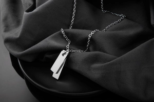 Polished silver stainless steel necklace with double bar pendants on grey fabric background