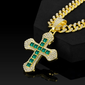 Macro view of gold hip hop cross pendant with green square gems and cuban chain link