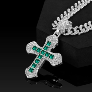 Macro detail of silver cross pendant with emerald square gems and cuban link chain