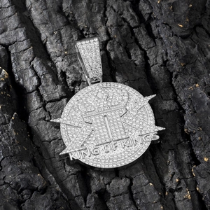 Macro shot of silver hip hop pendant with KING OF KINGS engraving on dark wood background