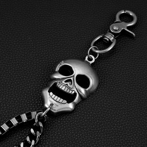 Detail of gothic silver skull keychain with lobster clasp on black leather background