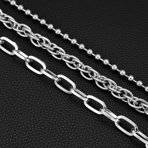 Detailed close-up of three layered silver stainless steel chains on black leather background