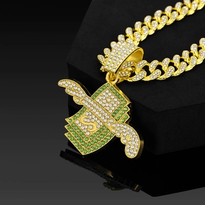 Détail d'un pendentif hip-hop doré avec ailes dollar et pierres vertes sur chaîne