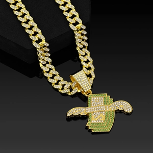 Détail d'une chaîne Cuban link dorée avec pendentif dollar ailé et cristaux verts brillants