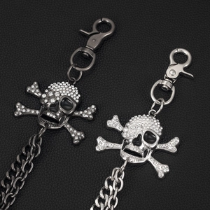 Close-up of punk skull trousers chain with rhinestone eyes on black leather background