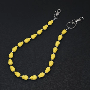 Detail of yellow skull charm chain with silver hardware on black leather background
