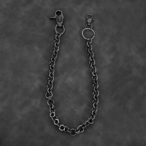 Macro detail of gunmetal industrial trousers chain featuring skull clasp and hex nut links