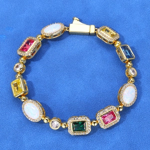 Hip hop gold bracelet featuring multicolored gemstones and white opals on blue felt background