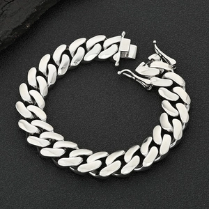 Detailed macro view of polished silver Cuban link chain bracelet on a black textured surface