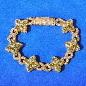 Macro detail of gold Cuban chain bracelet featuring green clover gems and diamond buckle