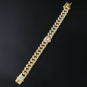 Macro shot of gold Cuban link bracelet featuring iced-out pink heart and crystal clusters