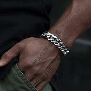 Nahaufnahme eines polierten Edelstahl-Panzerarmbands an einem tätowierten Handgelenk