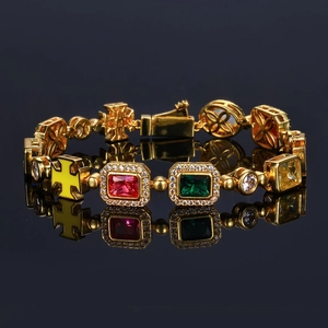 Détail macro d'un bracelet doré avec gemmes multicolores et breloques croix sur miroir noir