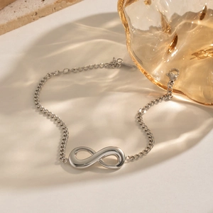 Detail of silver infinity symbol bracelet with Cuban chain on a textured stone surface