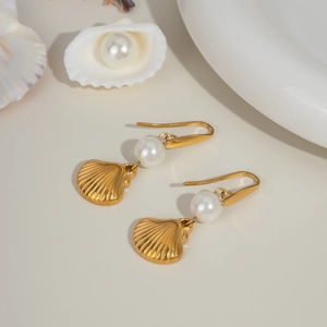 Close-up of gold shell earrings with white pearls featuring textured scallop pendants