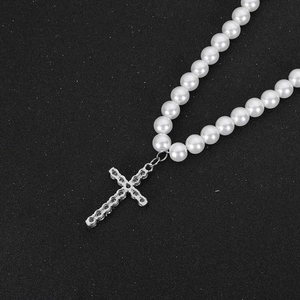 Minimalistische Perlenkette mit einem Strass-Kreuzanhänger auf dunklem Grund