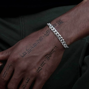Detail of silver Cuban link bracelet on wrist with tattoos showing high-polish finish