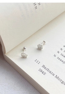 Macro shot of S999 silver cat paw and fish stud earrings resting on an open book page