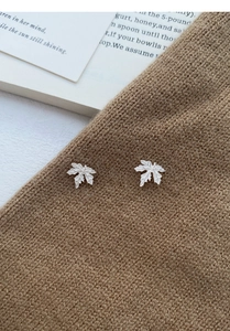Vue détaillée de boucles d'oreilles feuille d'érable argentées sur tissu tricoté