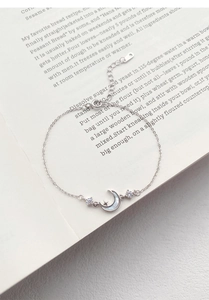 Detail shot of S999 sterling silver moon and star bracelet on a minimalist book background