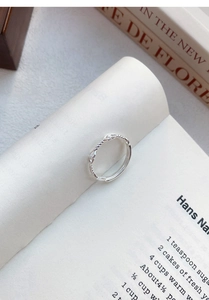 Dettaglio dell'anello a nodo d'argento intrecciato con texture metallica su un libro