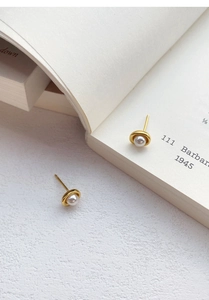 Nahaufnahme eleganter S925 Silber Perlenohrstecker mit goldener U-Fassung auf einem Buch