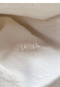 Close-up of S999 silver heart stud earrings with tulip floral detail on linen