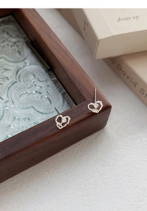 Detailed close-up of S999 silver hollow heart and rose stud earrings on vintage glass