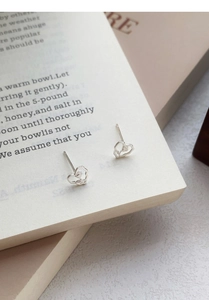 Macro detail of S999 silver heart stud earrings with rose design on a book page